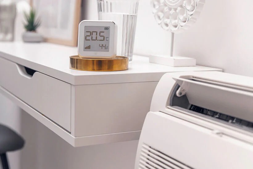 Sensor de temperatura y humedad sobre un mueble, junto a un aire acondicionado